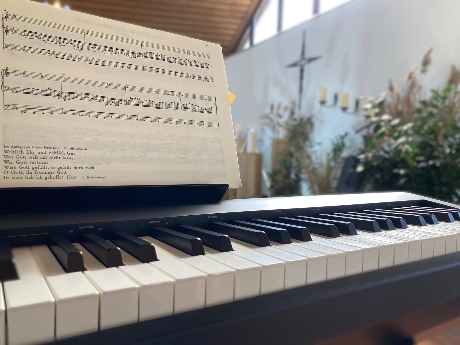 Orgelmusik für Trauerfeiern: Notenblatt auf einem Digitalpiano in einer hellen Trauerhalle mit Kreuz